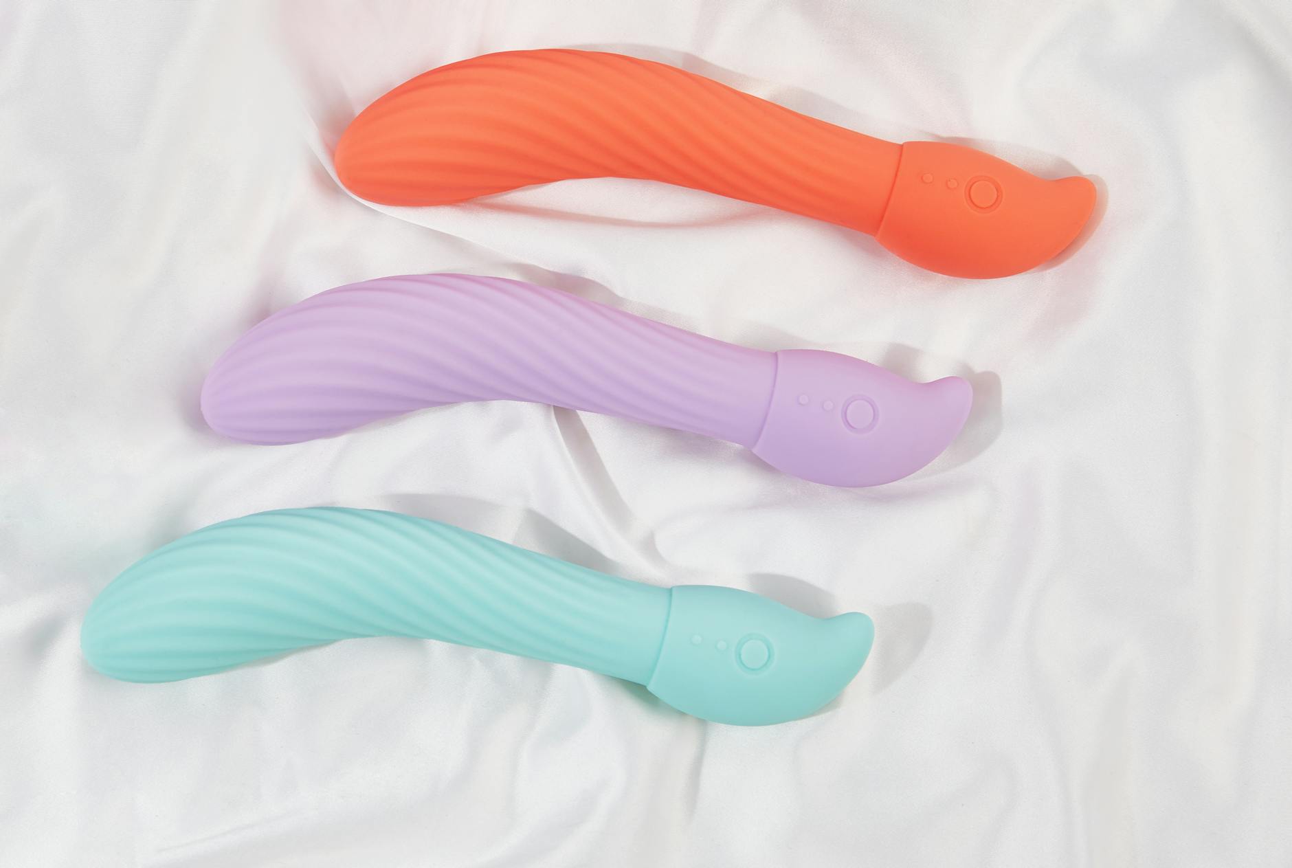 Three colorful vibrators arranged on white silk fabric, highlighting smooth texture and design.