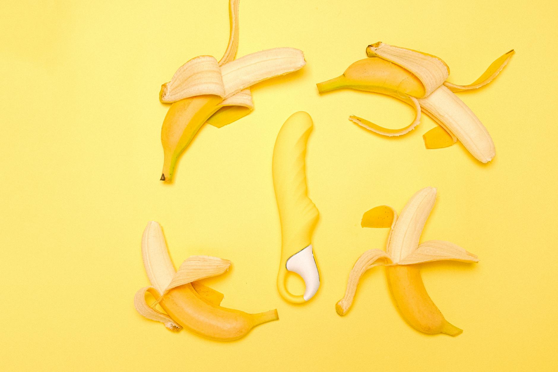 A yellow silicone lemon vibrator surrounded by fresh lemons on a bright yellow background