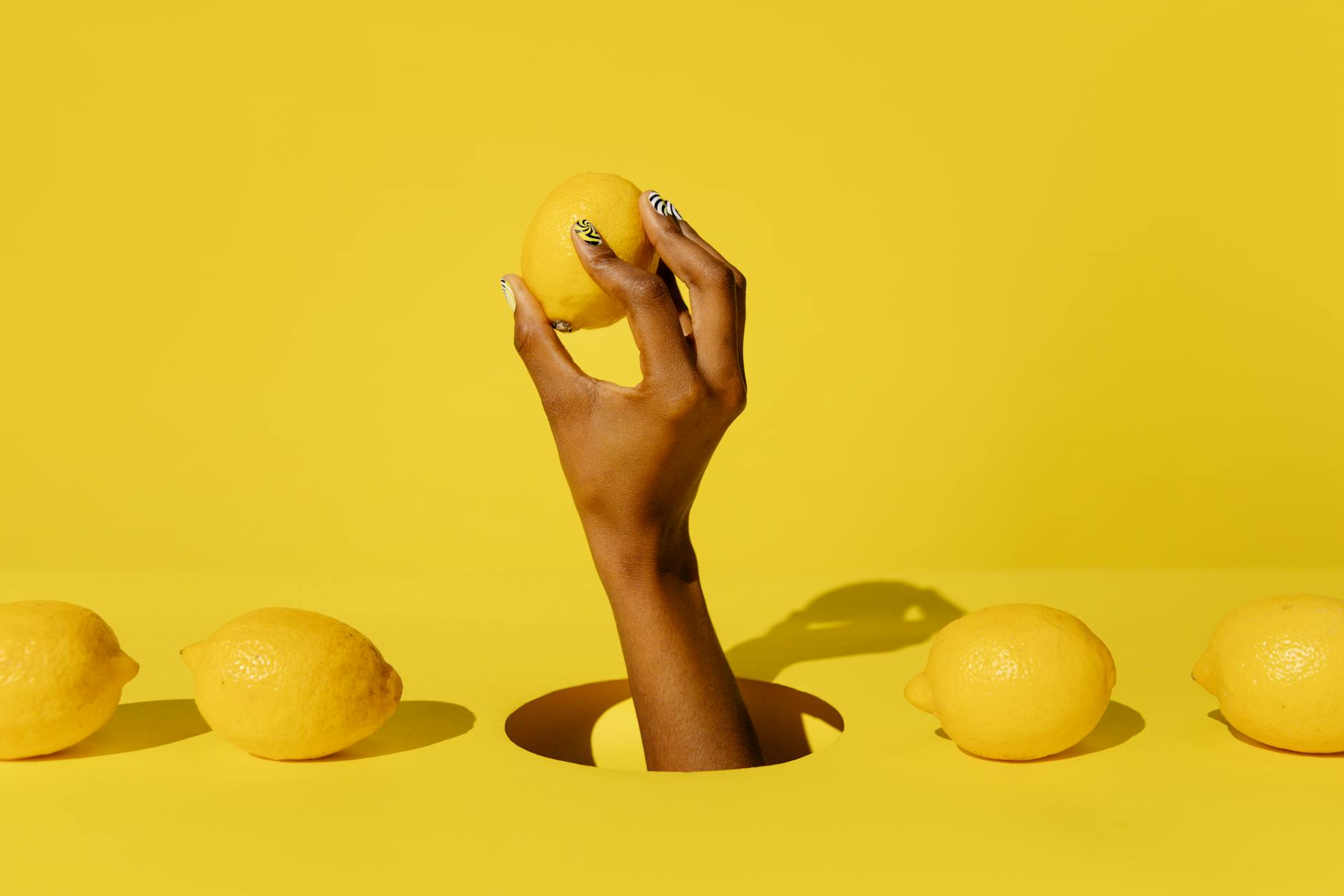 Hand holding a fresh lemon against a bright yellow background, symbolizing the fresh approach to pelvic health and pleasure