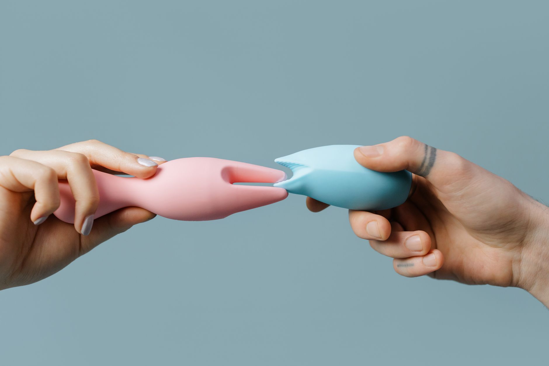 Hands holding pastel-colored silicone clitoral vibrators