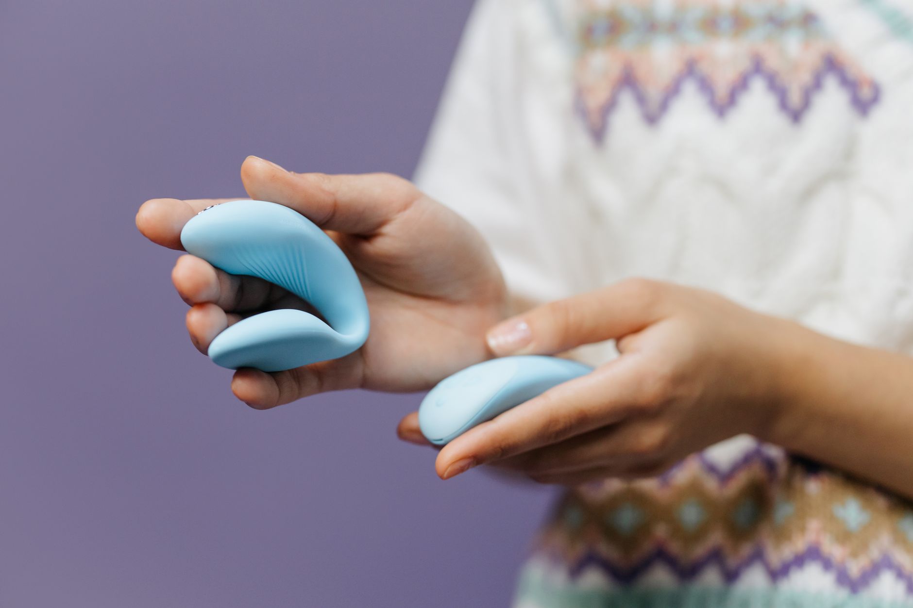 Close-up of hands holding a sleek lemon vibrator against a purple background