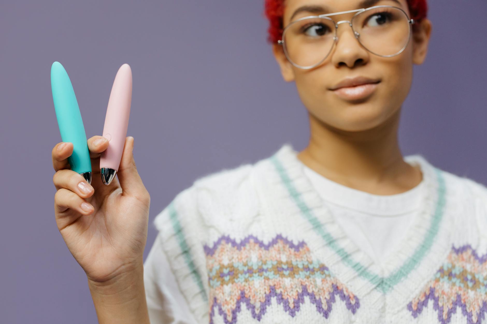 Two colorful vibrators held against a purple background, representing diverse pleasure needs and solutions.