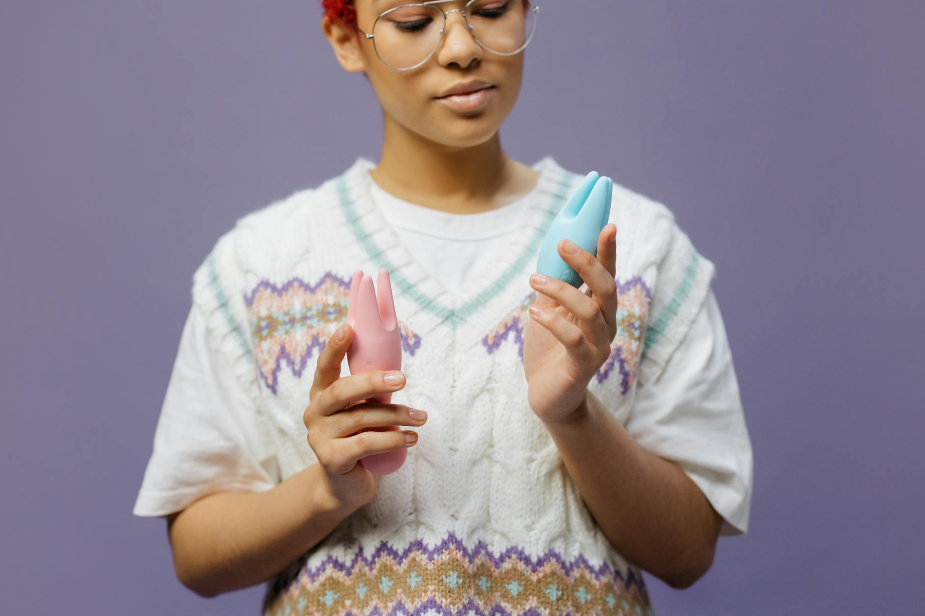 Person holding blue and pink silicone vibrators in a thoughtful, contemplative pose.