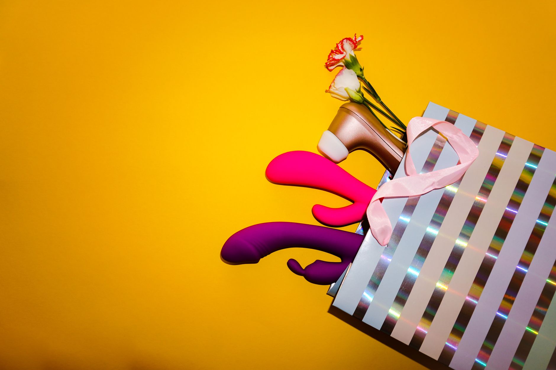 Colorful vibrators displayed in a holographic gift bag against a bold yellow background