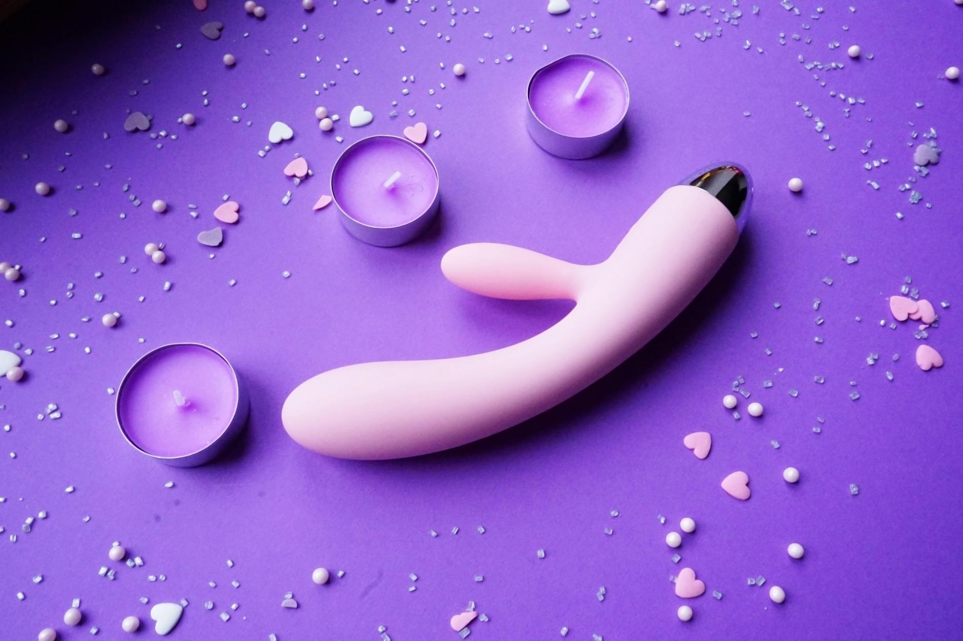 Pink lemon vibrator on purple background with heart confetti and candles for intimate pleasure